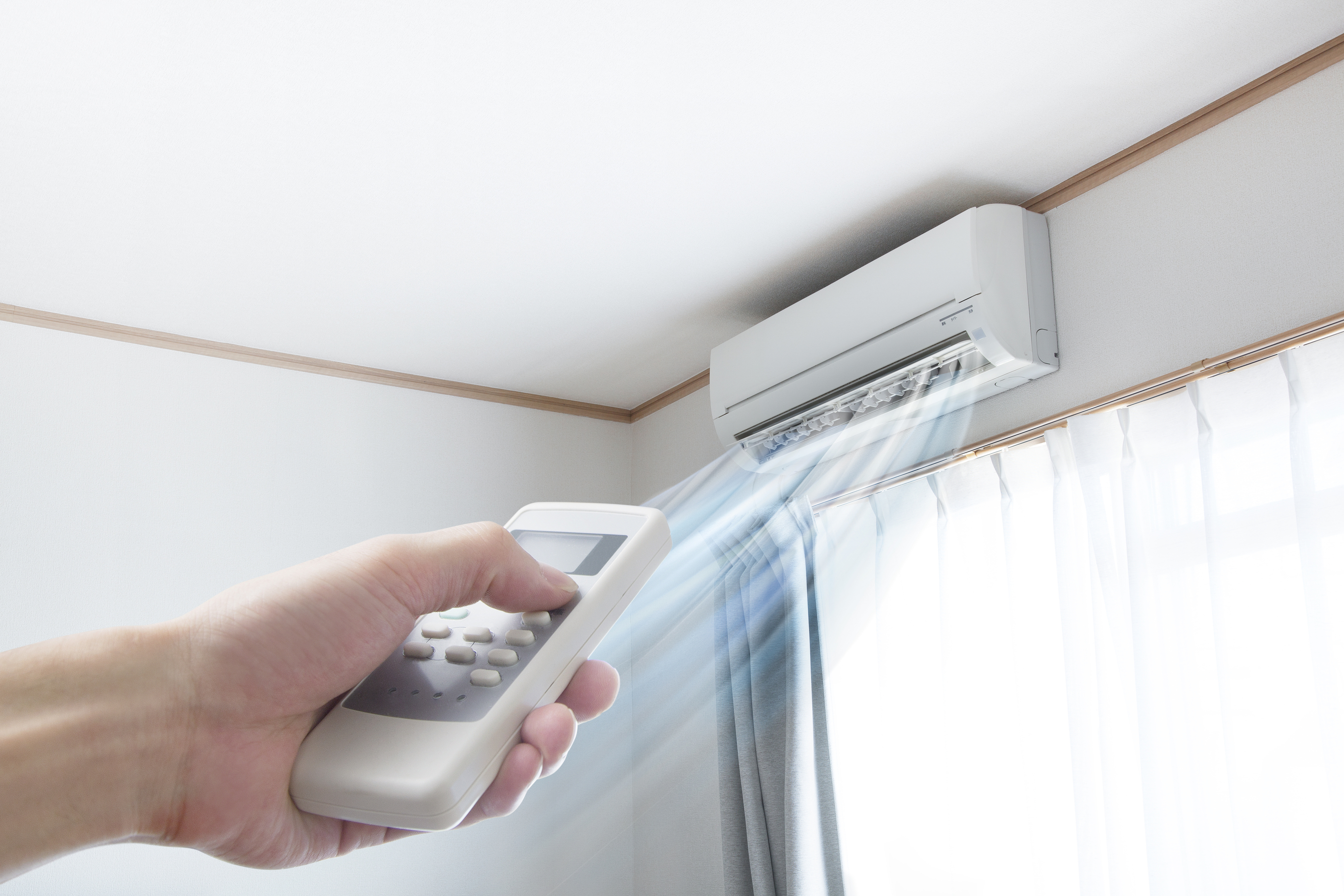 Hand pointing a remote at a ductless mini-split that’s blowing cold air