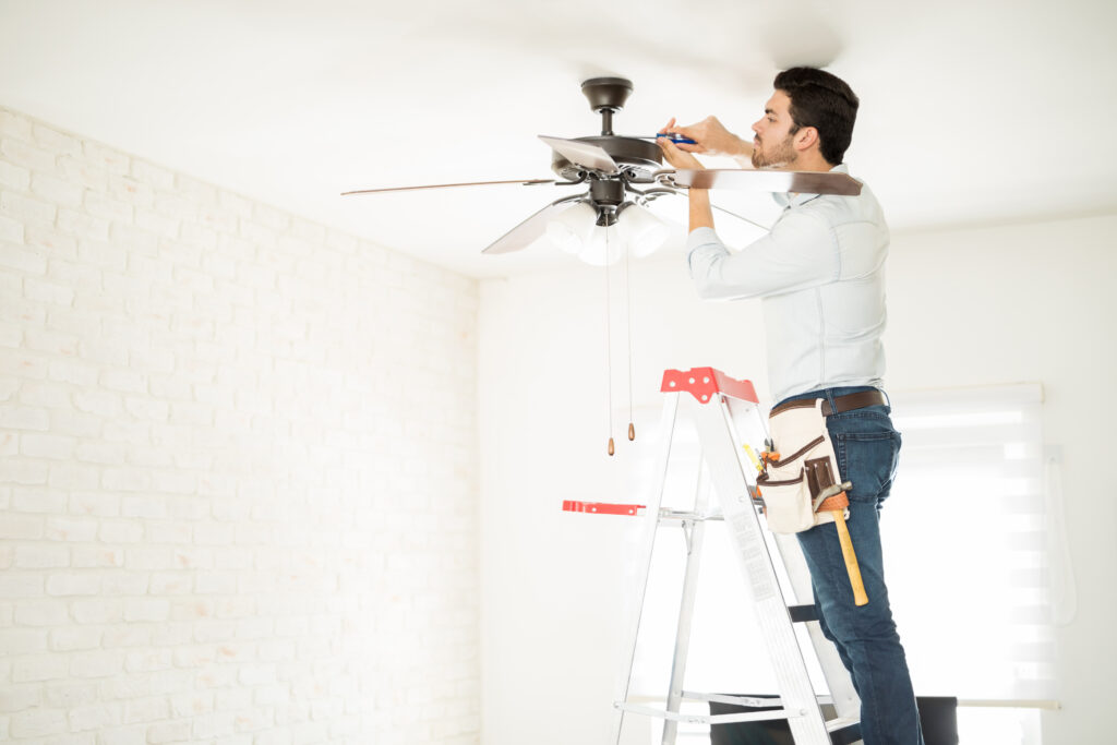 Electrician on a ladder fixing a ceiling fan in residence